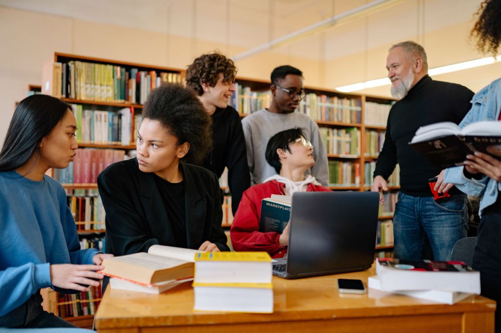 Stock photo of A diverse group of students studying together at a university library, engaged in discussion. https://www.pexels.com/photo/group-of-people-sitting-on-chair-in-front-of-table-8199558/